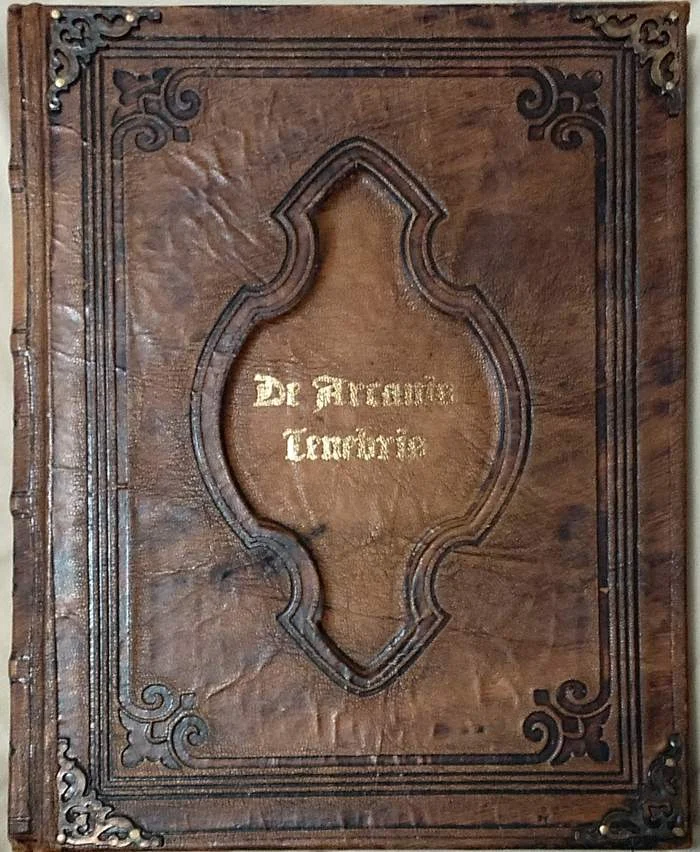 The cover of De Arcanis Tenebris: brown leather with a tooled frame, metal corners and the title stamped in gold